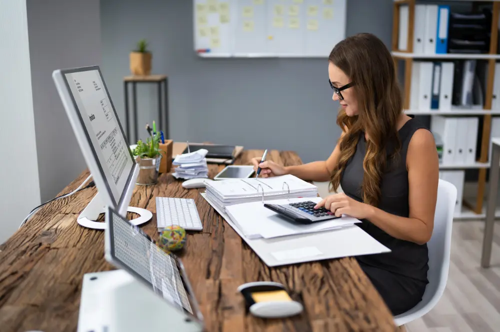 A woman calculates figures at her desk, focusing on direct indexing and tax loss harvesting strategies.