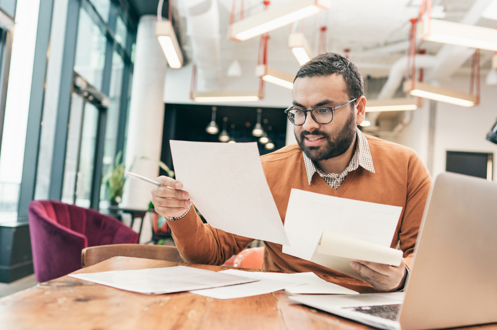 A man in a sweater and glasses reviews financial documents, symbolizing holistic financial planning and analysis.