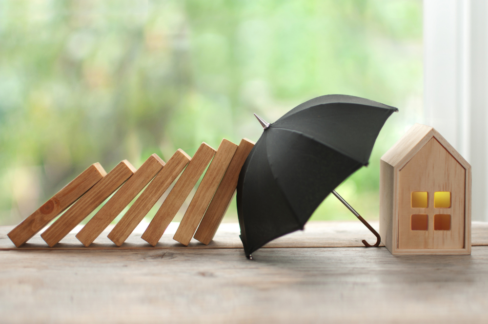 A tabletop scene featuring a house, an umbrella, and wooden blocks, representing the concept of umbrella insurance.
