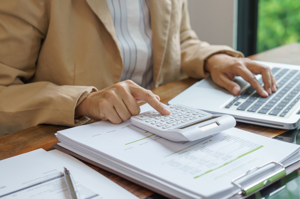 Individual engaged in tax loss harvesting, using a calculator and laptop for financial analysis.
