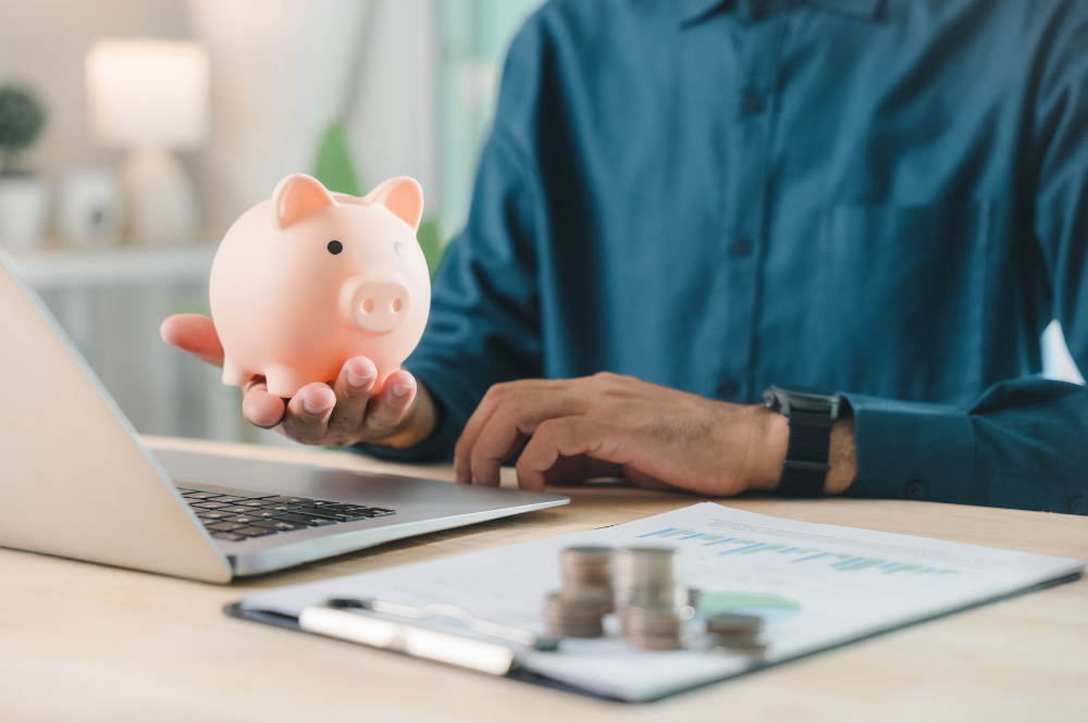 Man holding a piggy bank on a desk with a laptop, symbolizing retirement income planning and financial management.